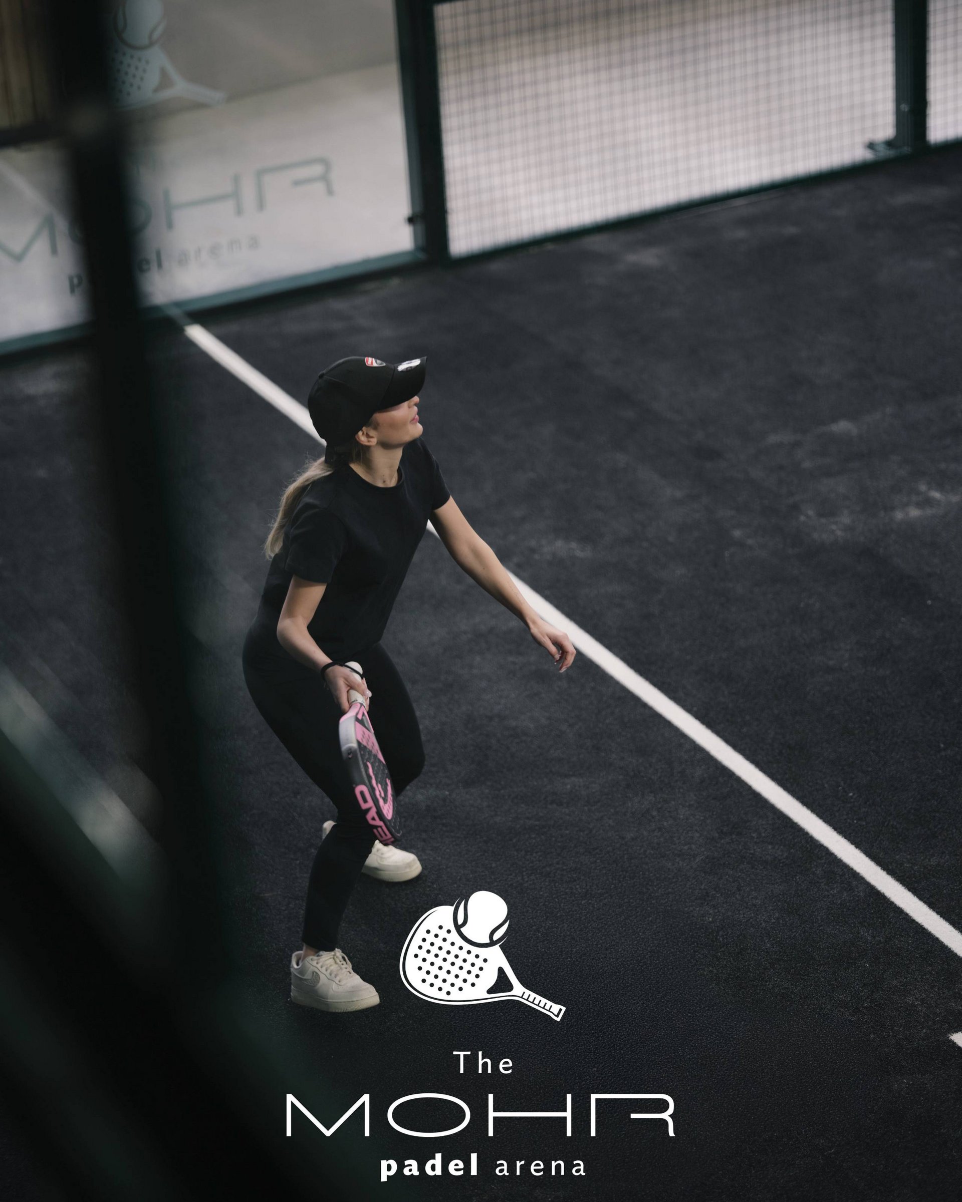 Frau spielt Padel auf dunklem Platz mit Schläger und Ball