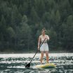 Frau steht auf Stand-Up-Paddleboard auf See vor Waldkulisse