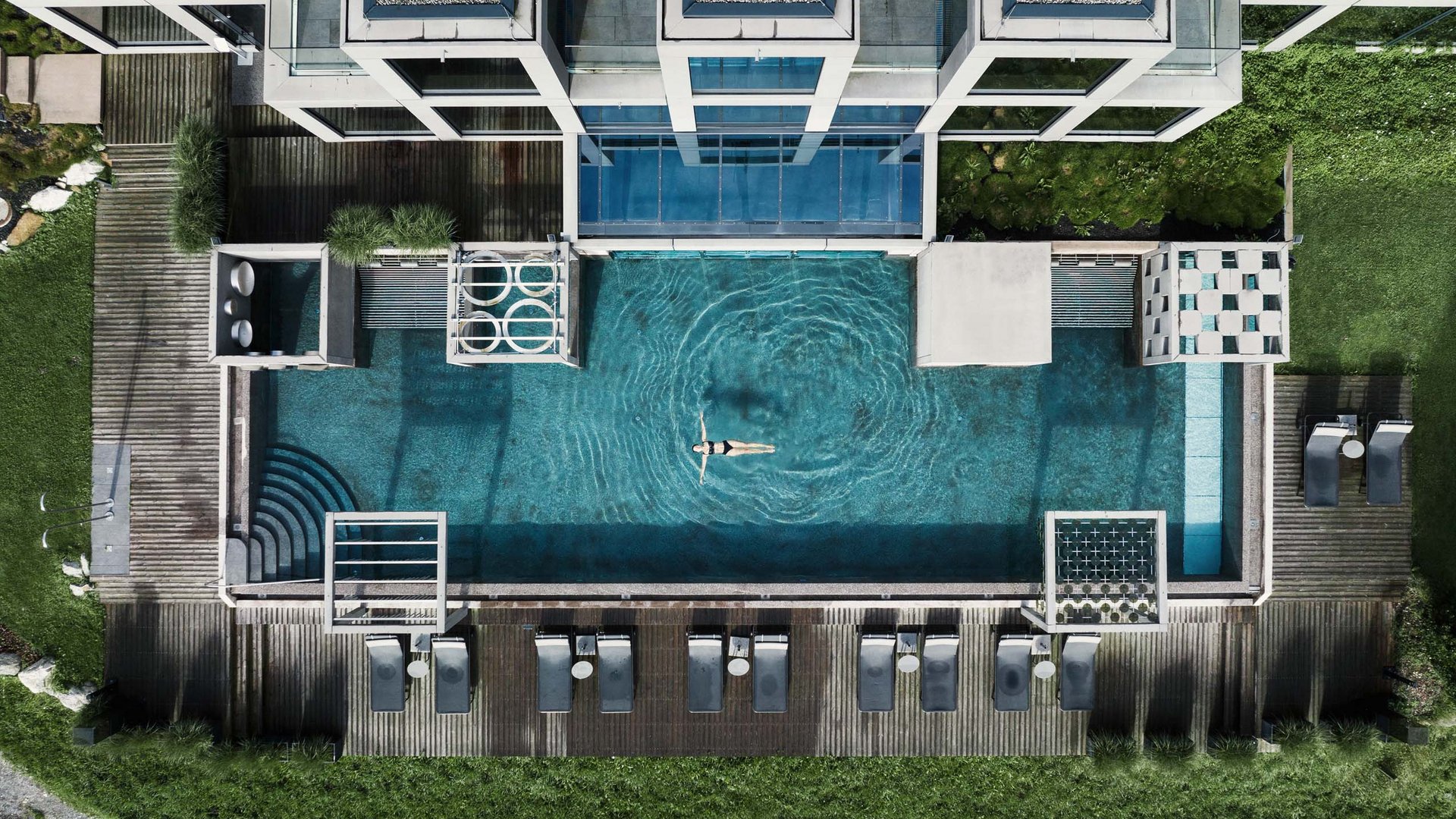 Drohnenaufnahme eines modernen Pools mit Person, die entspannt schwimmt