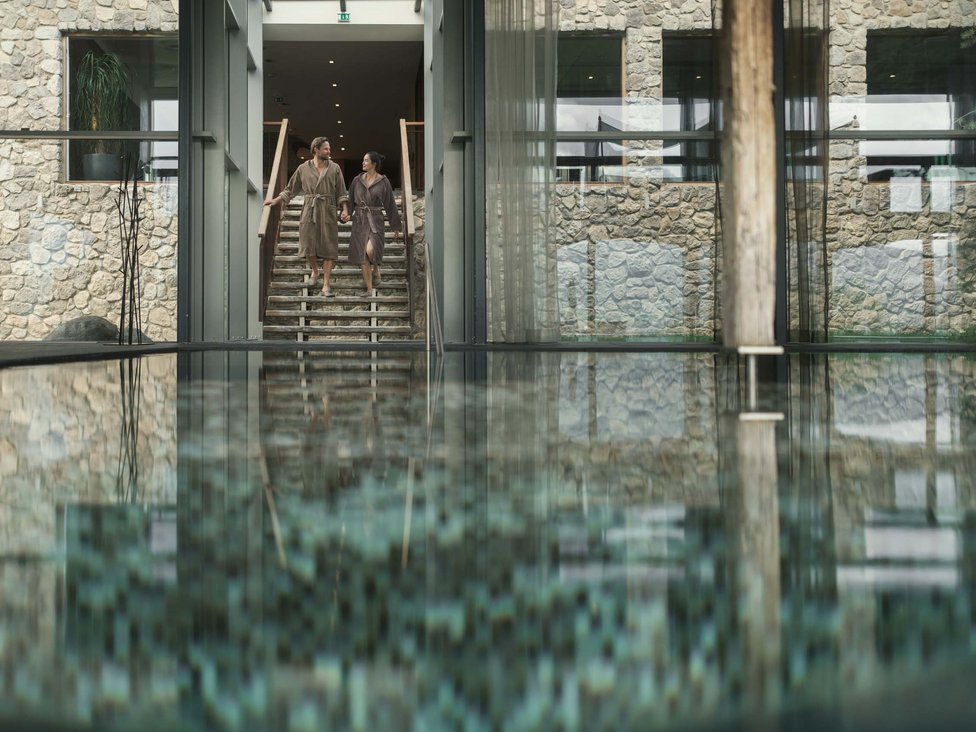 Paar in Bademänteln geht eine Treppe neben einem Innenpool in einem Spa