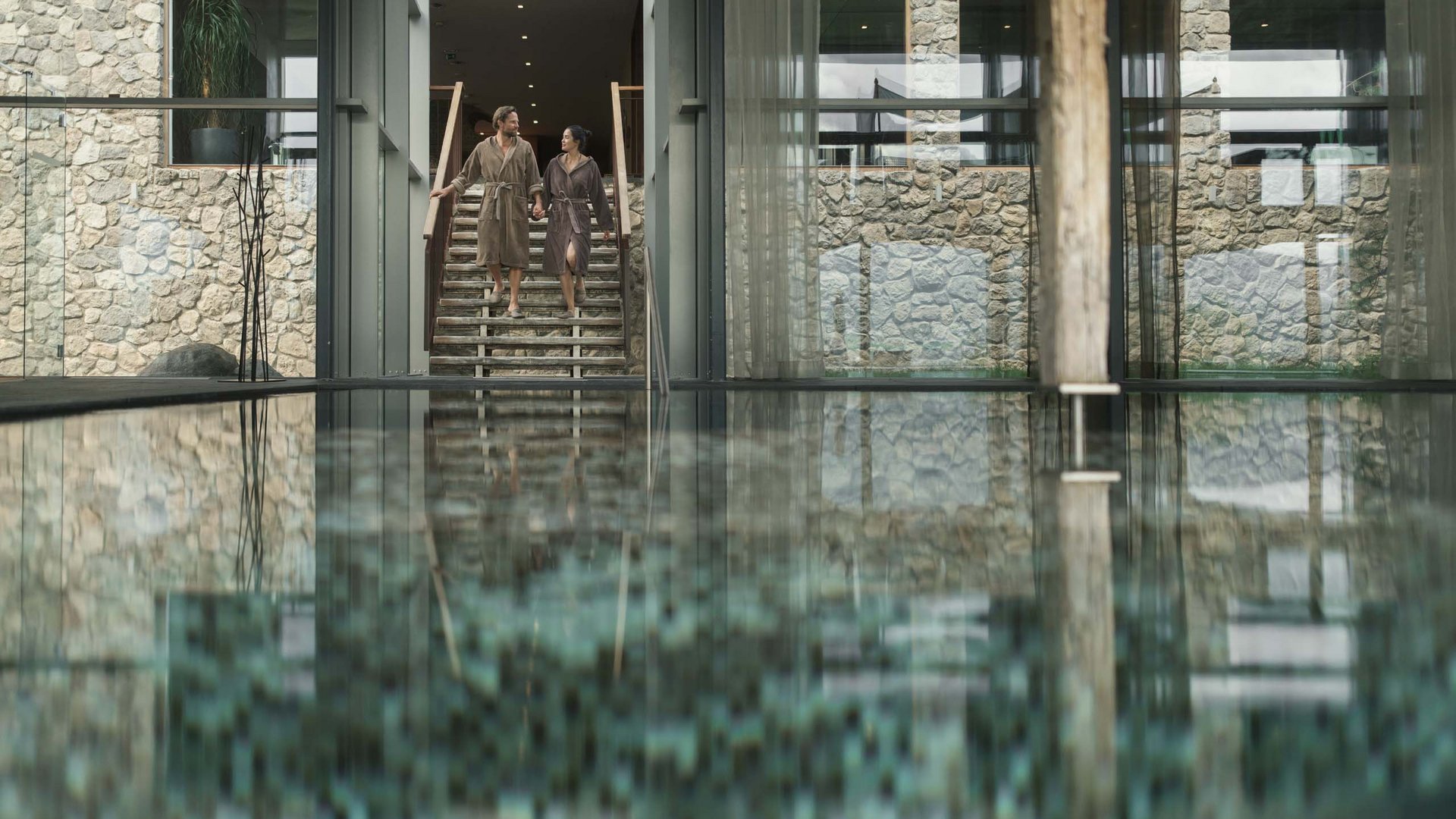 Paar in Bademänteln geht eine Treppe neben einem Innenpool in einem Spa