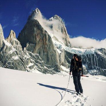 Bergsteiger mit Ausrüstung wandert durch verschneite Landschaft zu Felsgipfeln