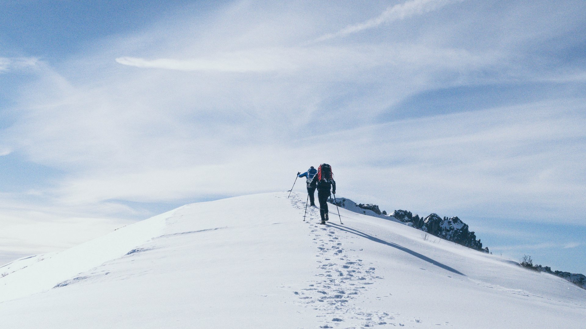 Wunderbares Winterwandern in Lermoos Zwei Wanderer steigen mit Stöcken auf eine schneebedeckte Bergspitze bei blauem Himmel
