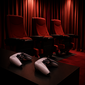 Zwei Spielcontroller auf einem Tisch vor drei roten Kinosesseln