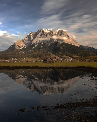 Wandern in und rund um Lermoos Berg mit Wolken und Spiegelung im Wasser vor einer Hütte und Dorf