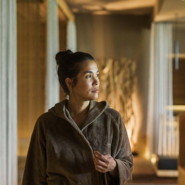 Frau im braunen Bademantel schaut nachdenklich in einem warm beleuchteten Raum