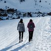 Zwei Personen wandern im Schnee vor schneebedeckten Bergen und Dorf