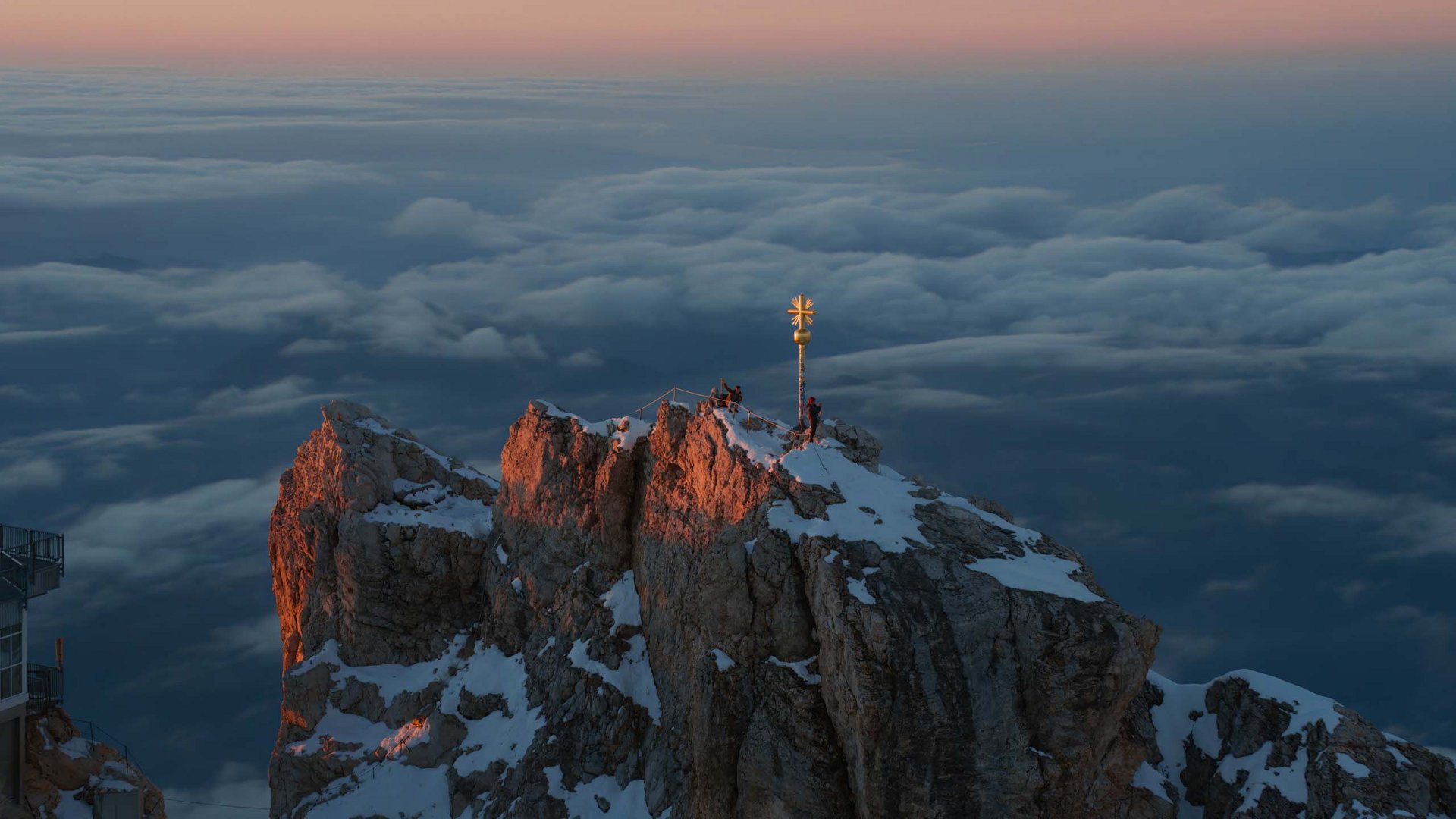 Gipfel eines schneebedeckten Bergs bei Sonnenaufgang mit Alpengipfelkreuz