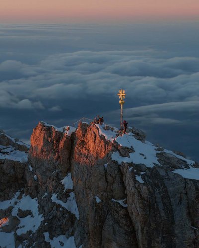 Gipfel eines schneebedeckten Bergs bei Sonnenaufgang mit Alpengipfelkreuz