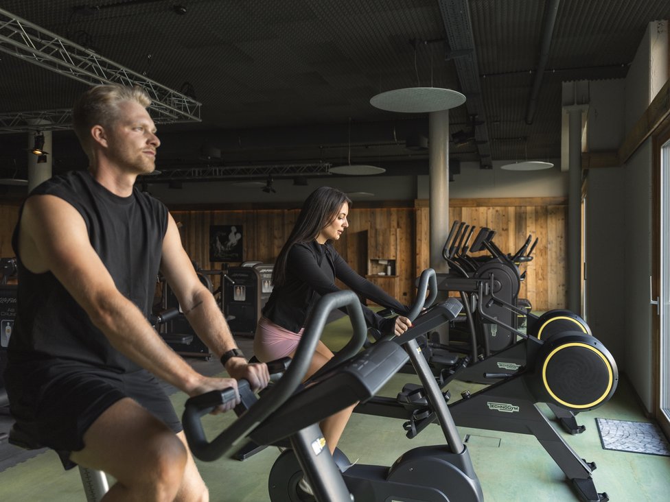 Mann und Frau trainieren auf Fahrradergometern im Fitnessstudio mit Holzverkleidung