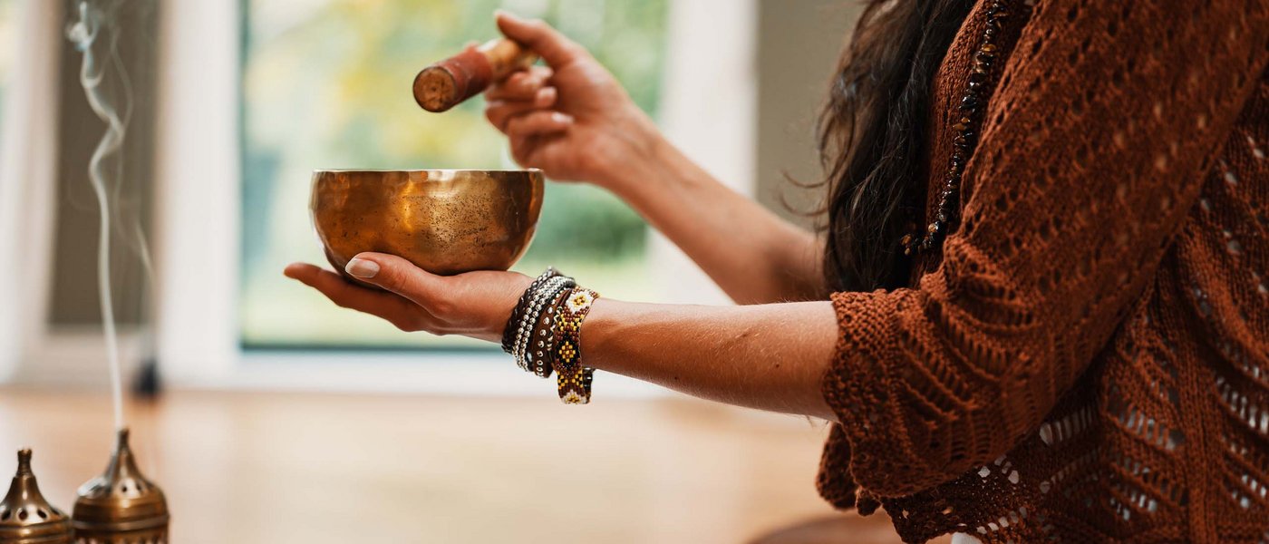 Frau meditiert mit Klangschale und Räucherstäbchen zu Hause