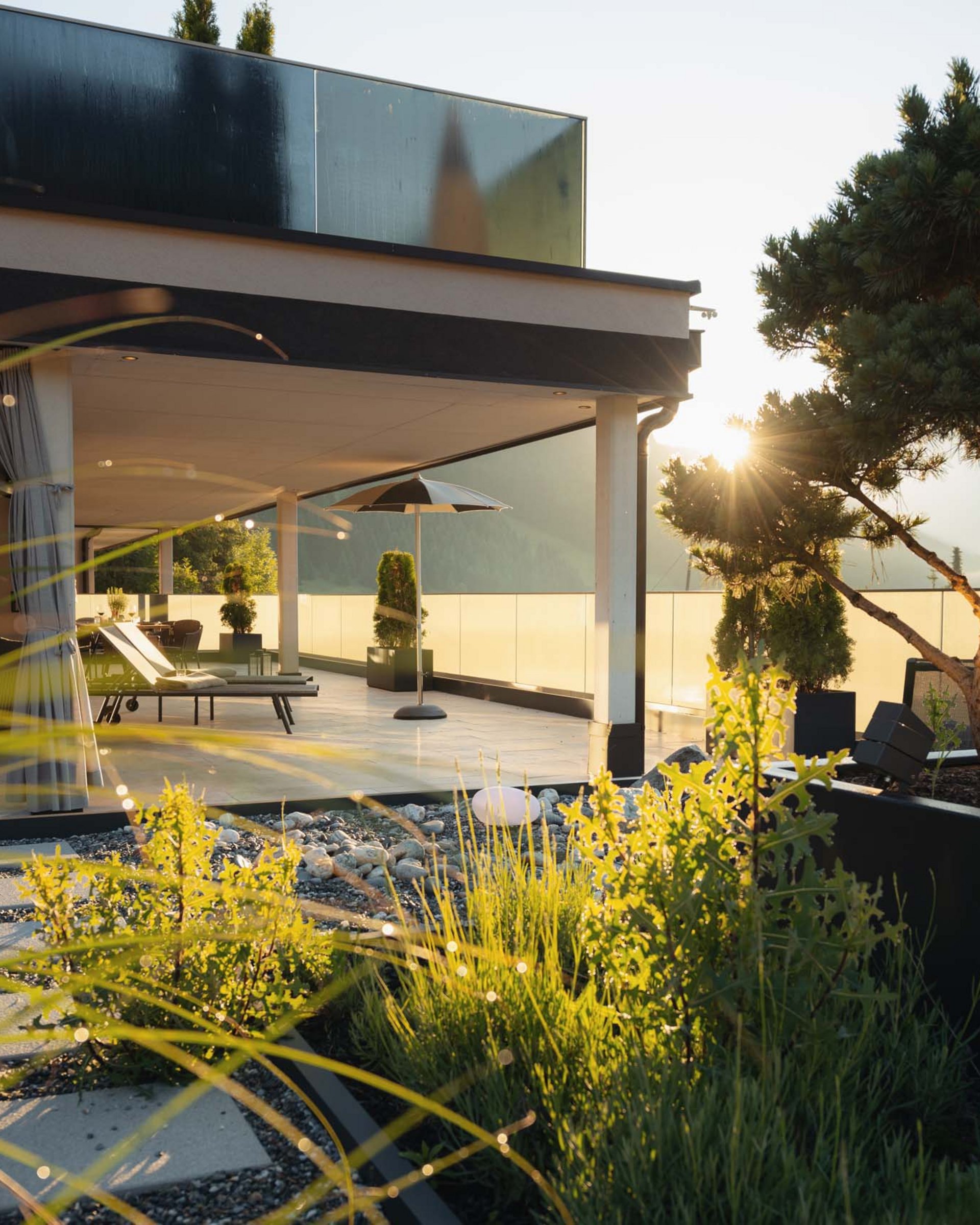 Moderne Terrasse mit Sonnenliegen und Pflanzkübeln bei Sonnenuntergang