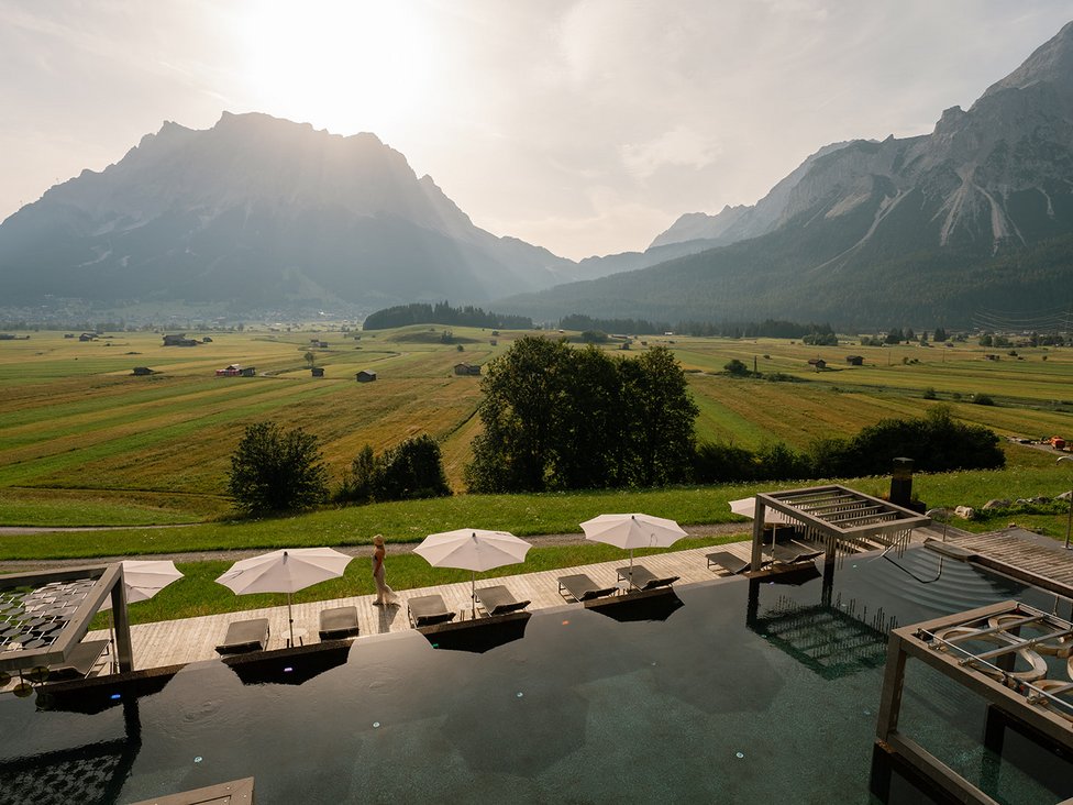 Pool mit Liegestühlen und Sonnenschirmen vor Berglandschaft im Sonnenlicht