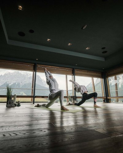Wellness und Luxus: Ihr Hotel in Tirol Zwei Personen machen Yoga vor großen Fenstern mit Bergblick