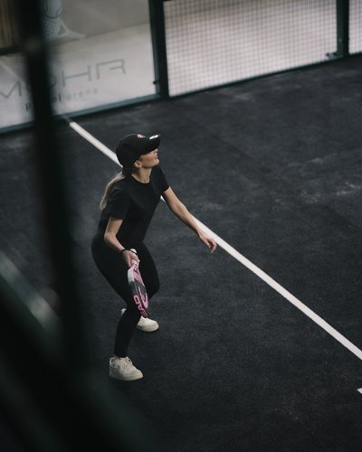 Frau spielt Paddle-Tennis auf einem schwarzen Sportplatz mit Schläger und Mütze