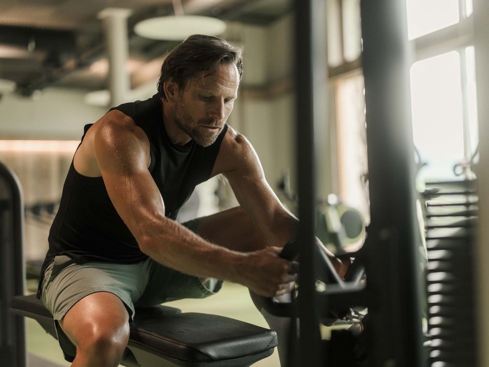 Wellness und Luxus: Ihr Hotel in Tirol Mann trainiert konzentriert an einem Kraftgerät im Fitnessstudio