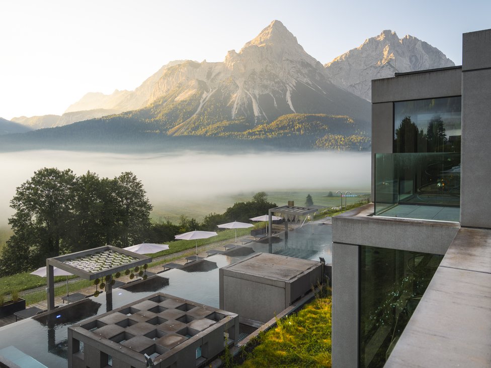 Blick auf Berglandschaft mit Nebel und modernem Hotelpool im Vordergrund
