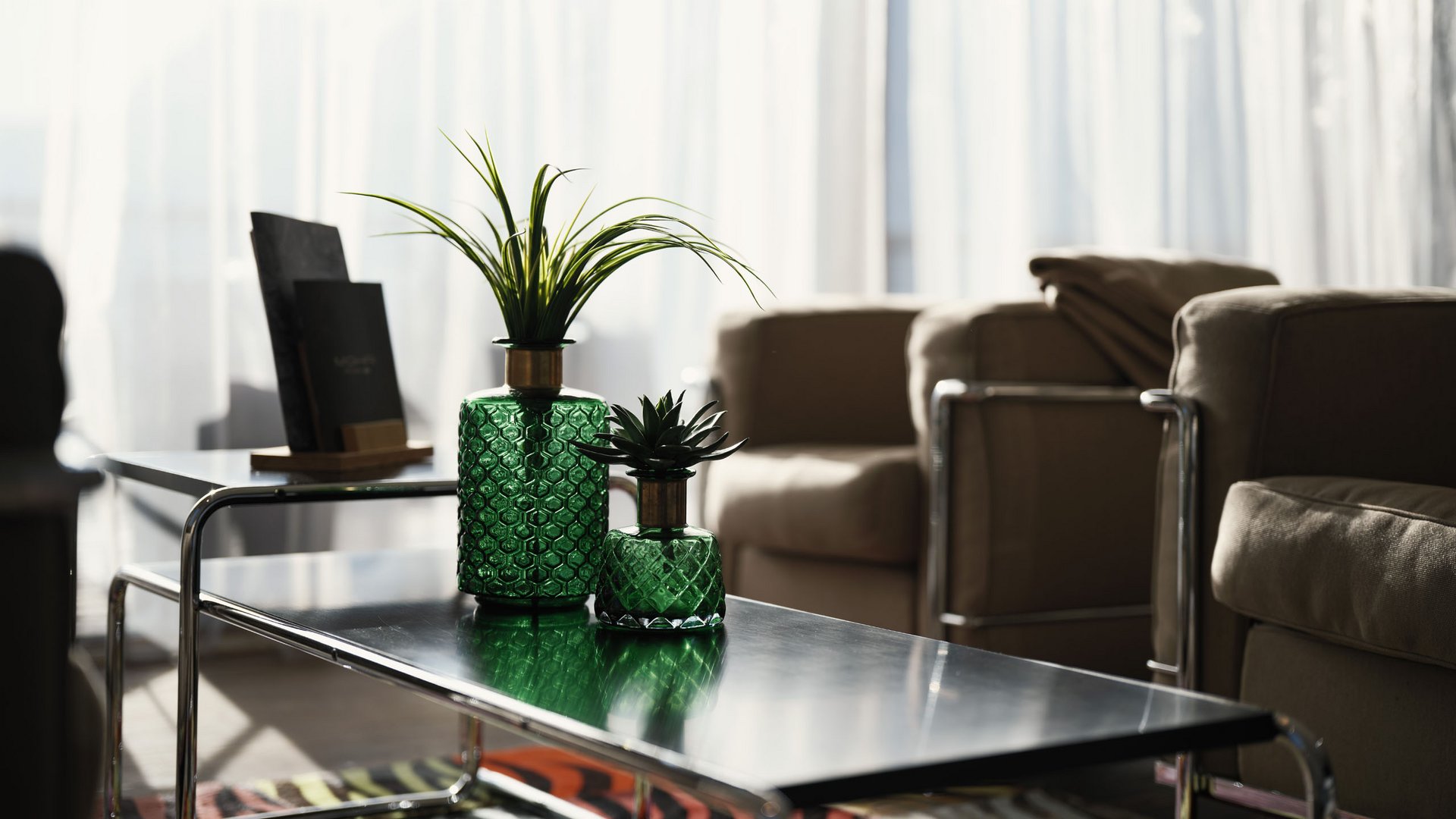 Grünes Glas mit Pflanzen auf modernem Tisch im Wohnzimmer mit Sesseln