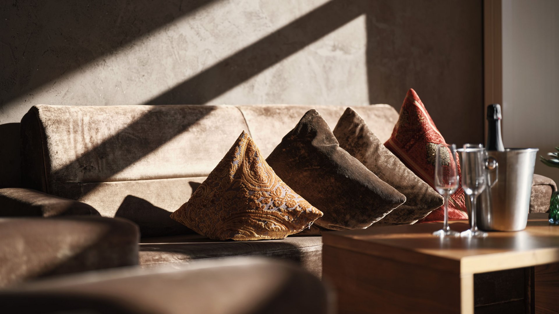 Sofa mit bunten Kissen und Champagner auf Holztisch im Sonnenlicht