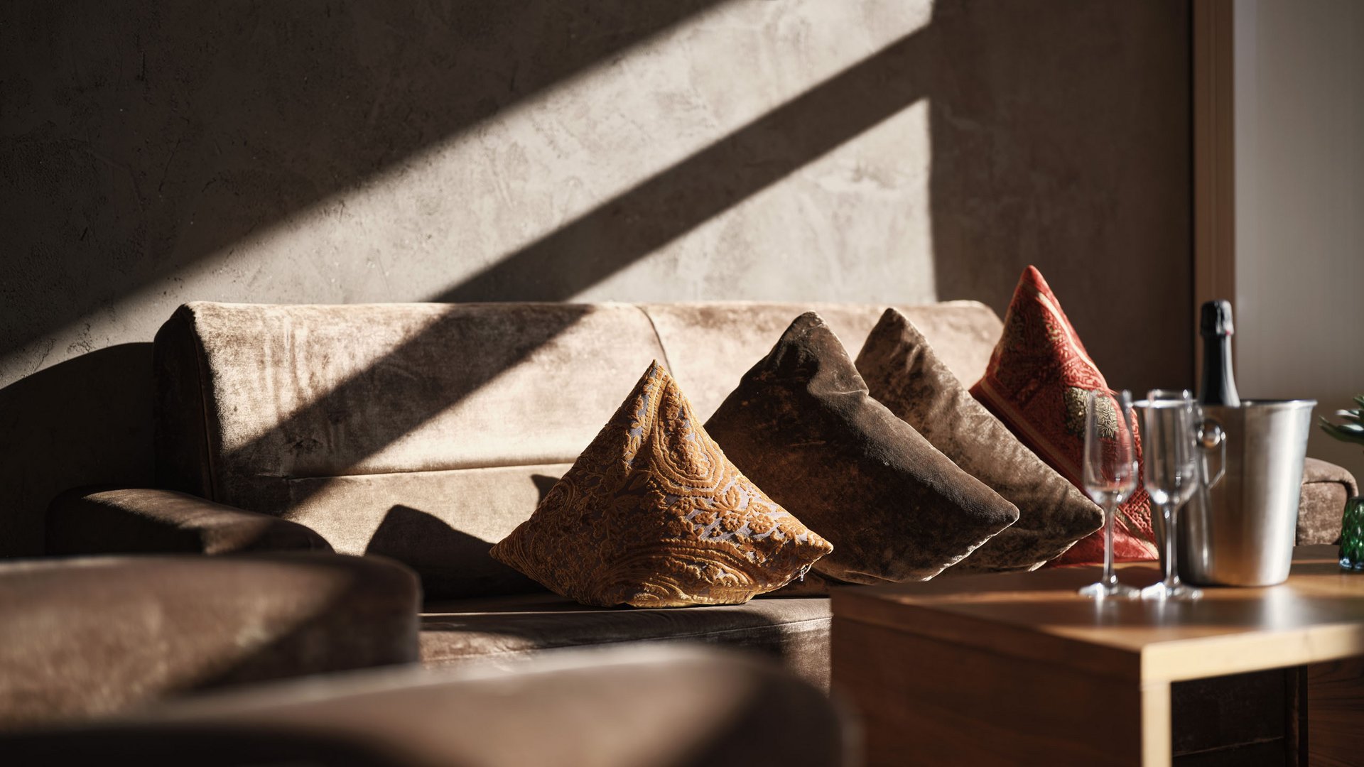 Sofa mit bunten Kissen und Champagner auf Holztisch im Sonnenlicht