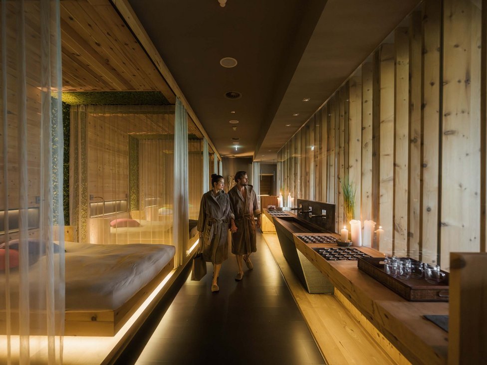 Ein Paar in Bademänteln geht durch einen warm beleuchteten Spa-Flur aus Holz.
