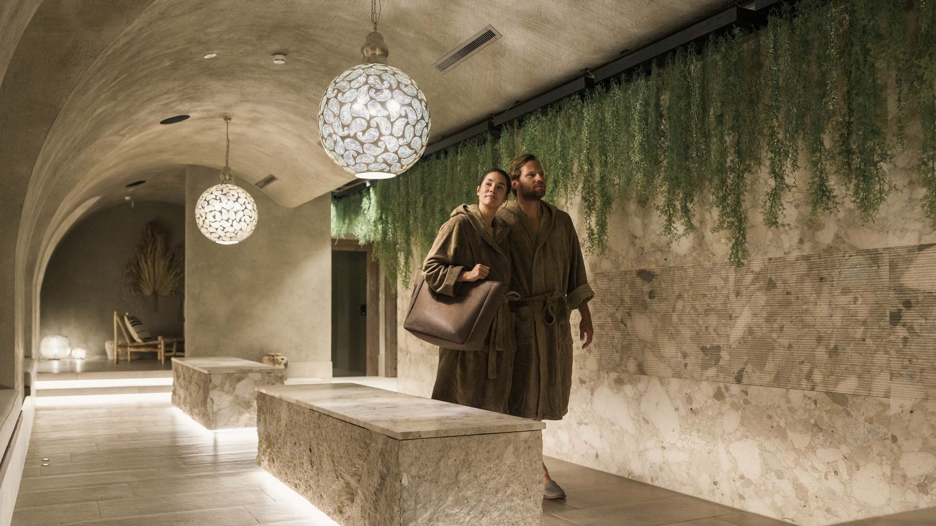Paar in Bademänteln in einem stilvollen Spa-Flur mit grünen Pflanzen und Beleuchtung