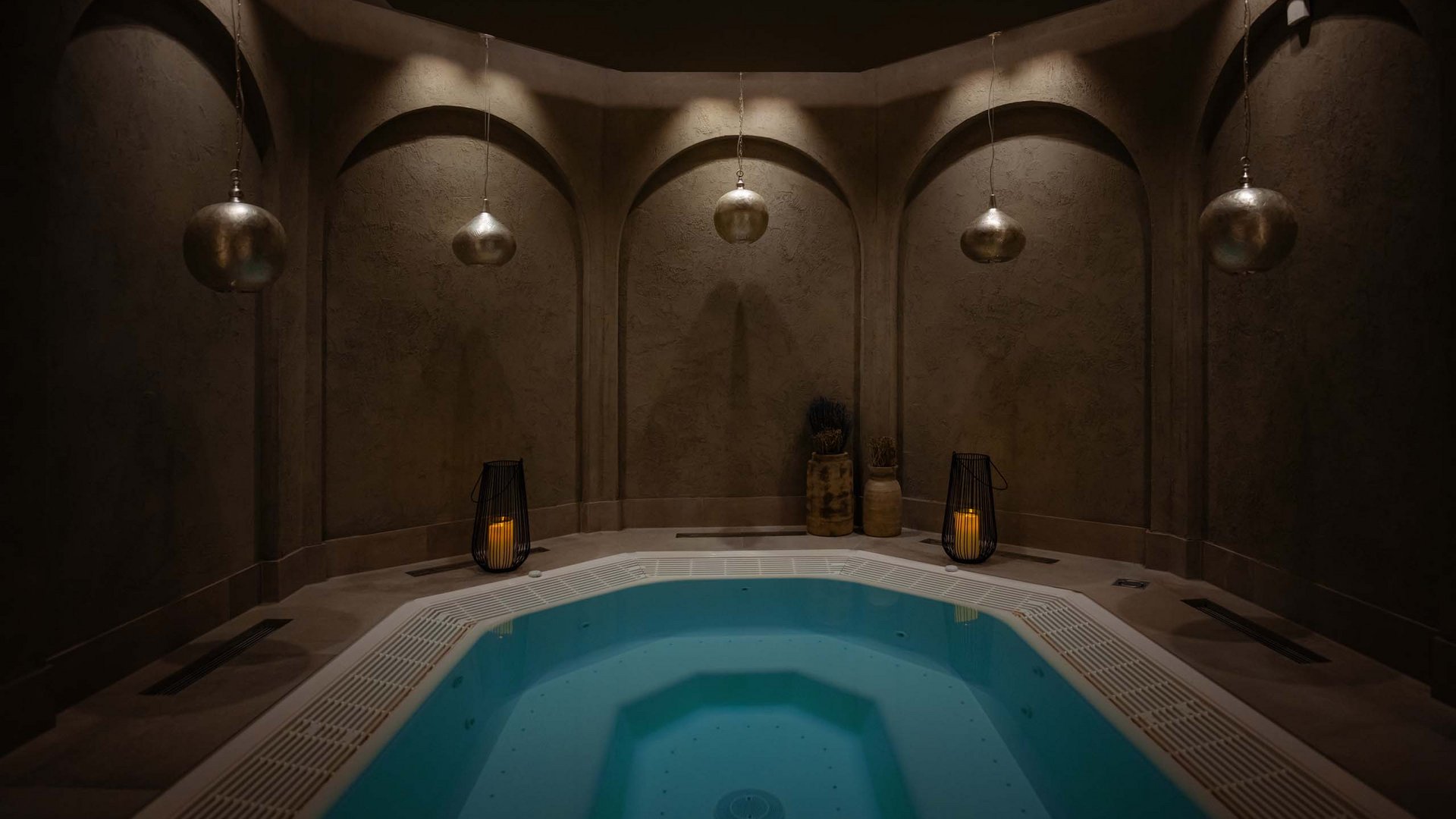 Lit hot tub in a dark round room with candles and hanging lamps