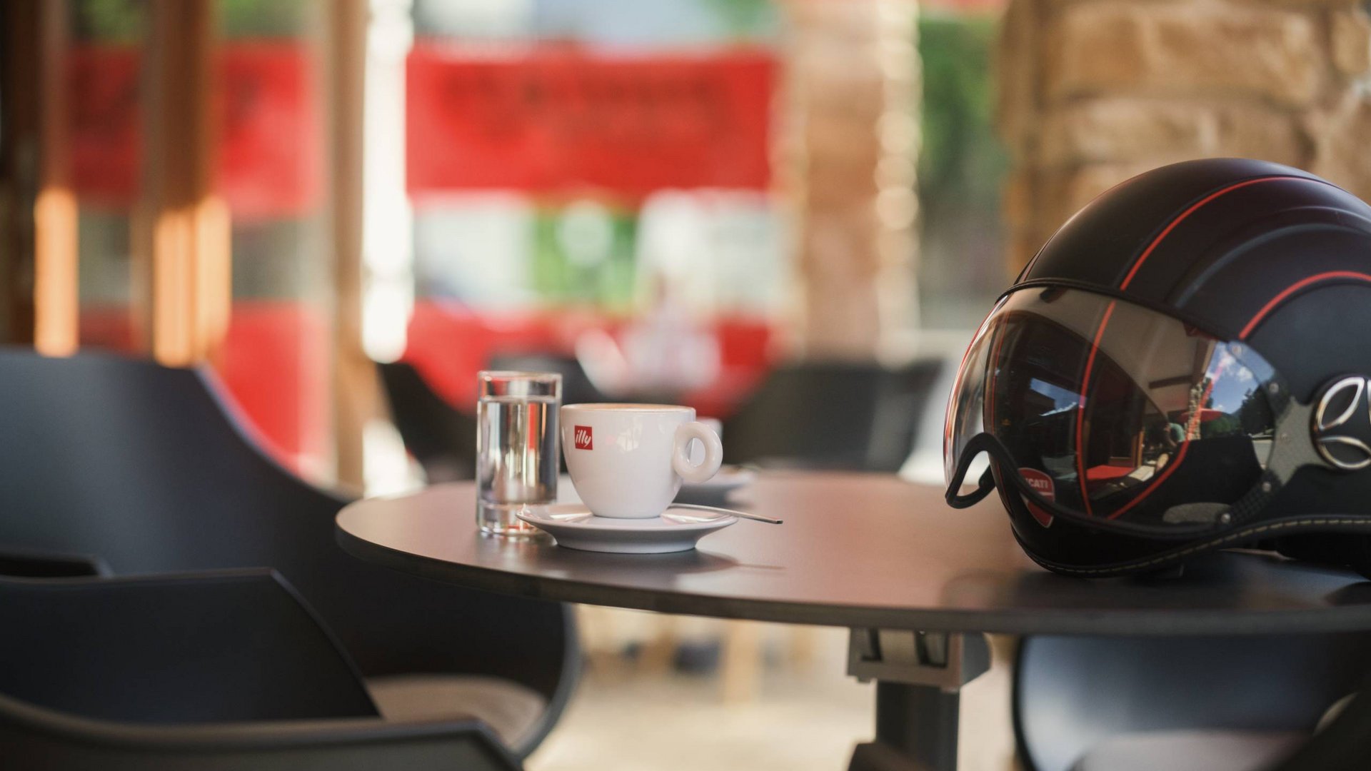 Kaffeetasse, Glas Wasser und Motorradhelm auf einem Cafétisch