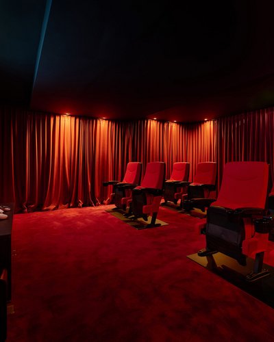 Kleines Heimkino mit roten Sitzen und rotem Teppich vor Leinwand