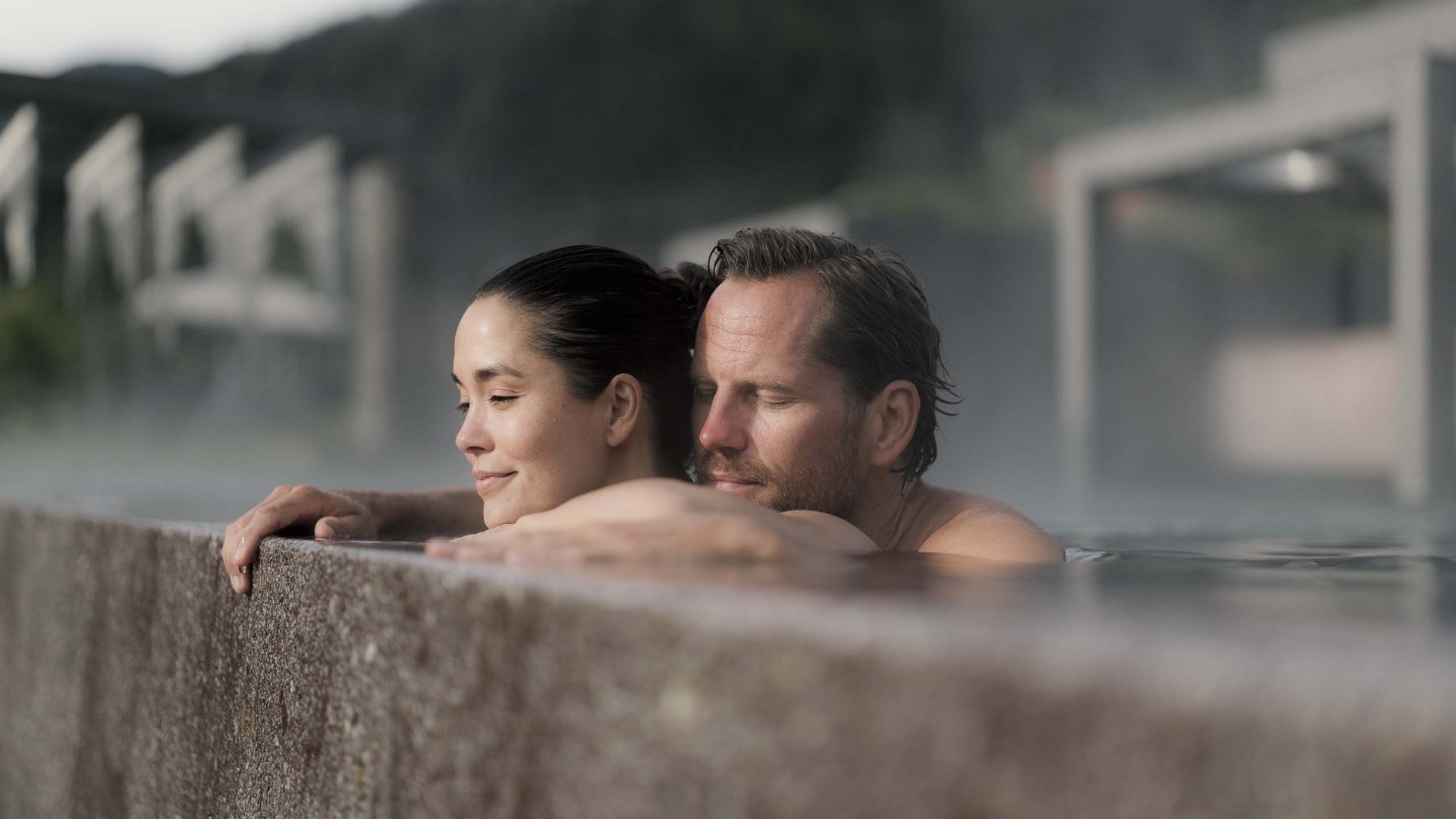 Paar entspannt im Pool am Beckenrand mit Hintergrund aus Bergen