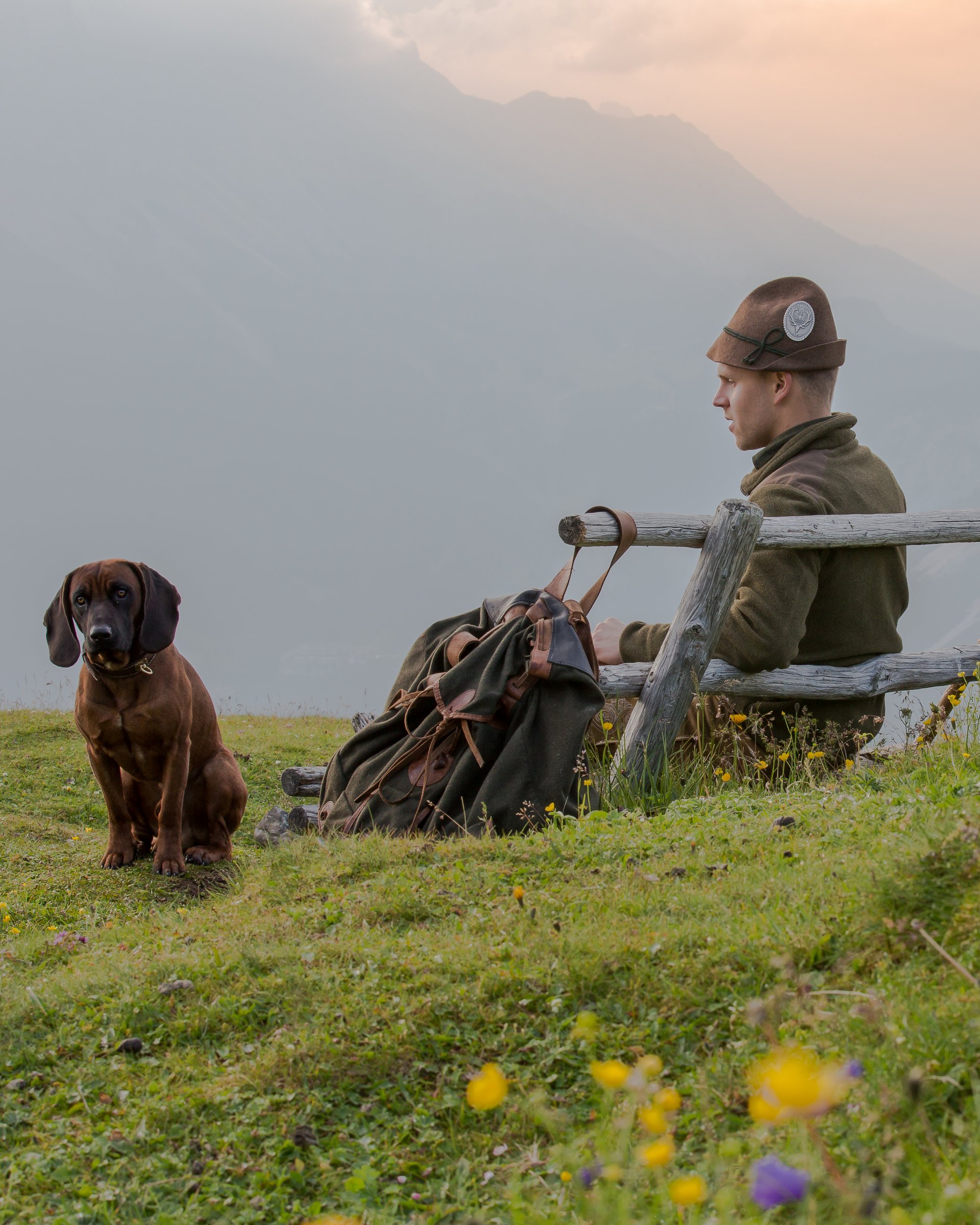 Jäger in traditioneller Kleidung sitzt auf Bank in den Bergen mit Hund
