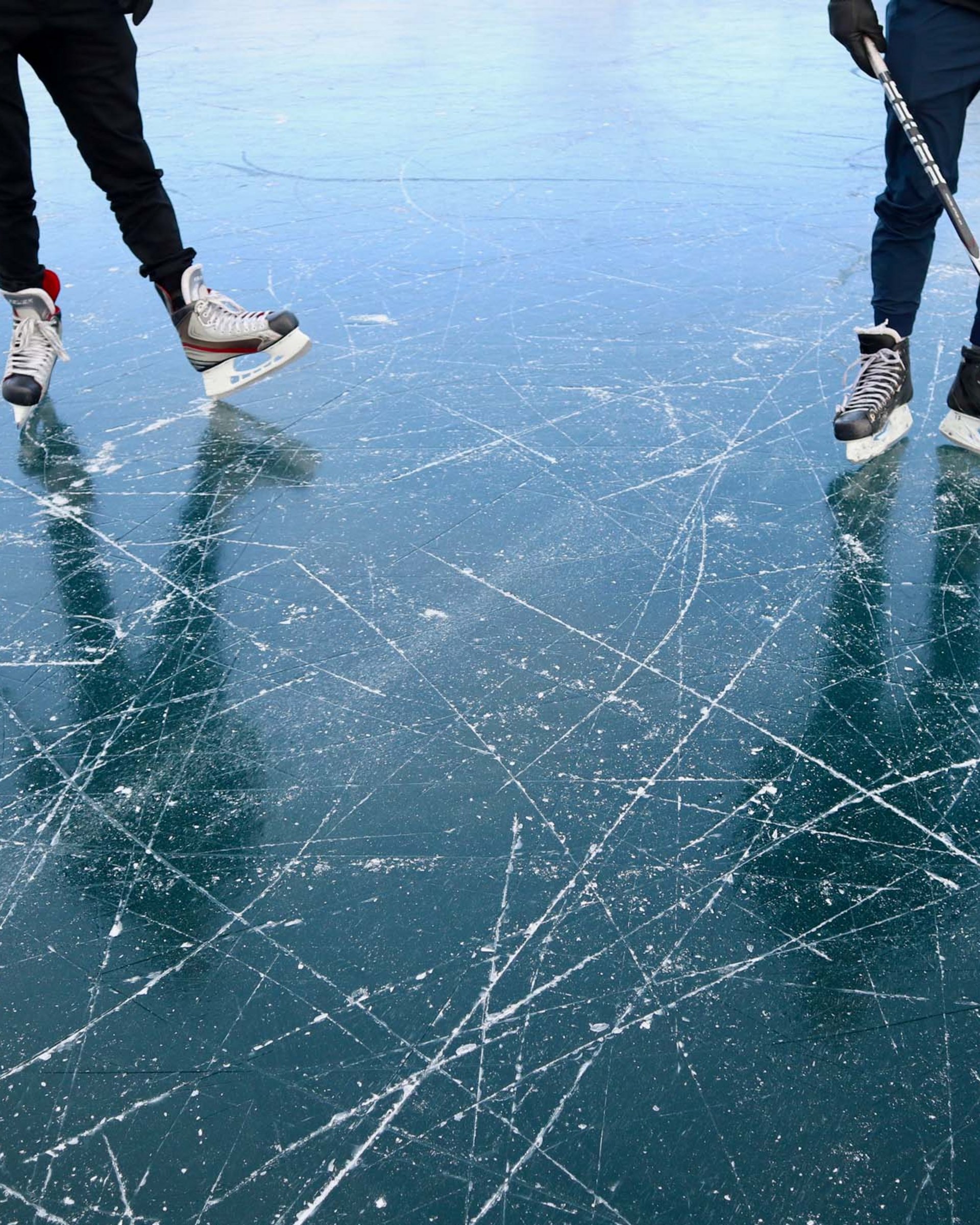 Drei Personen spielen Eishockey auf einer stark zerkratzten Eisfläche