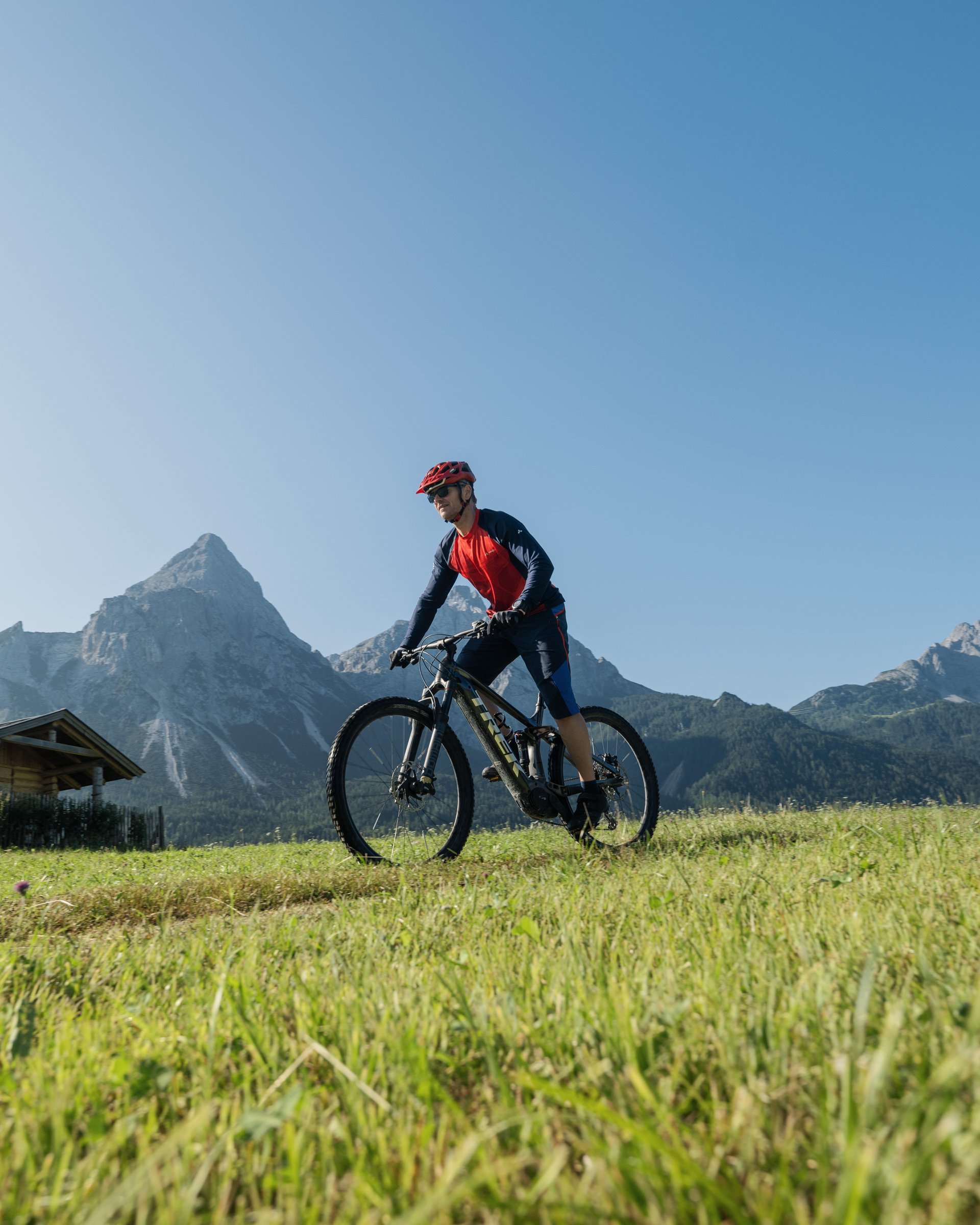 Mann fährt Mountainbike auf einer Wiese mit Bergkulisse bei klarem Himmel