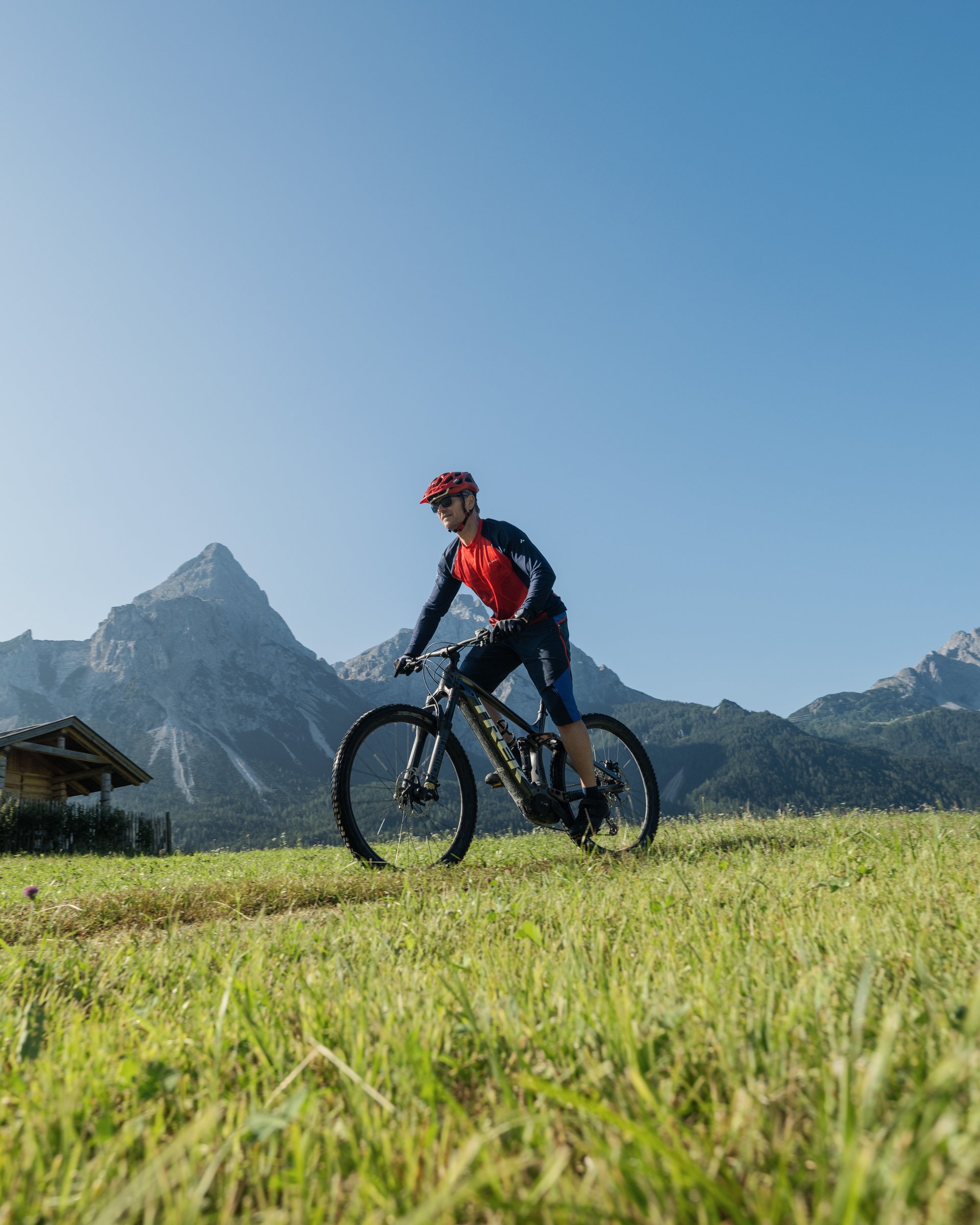 Mann fährt Mountainbike auf einer Wiese mit Bergkulisse bei klarem Himmel