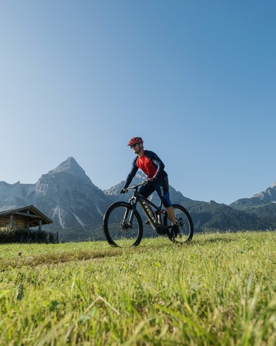 Wellness und Luxus: Ihr Hotel in Tirol Mann fährt Mountainbike auf einer Wiese mit Bergkulisse bei klarem Himmel