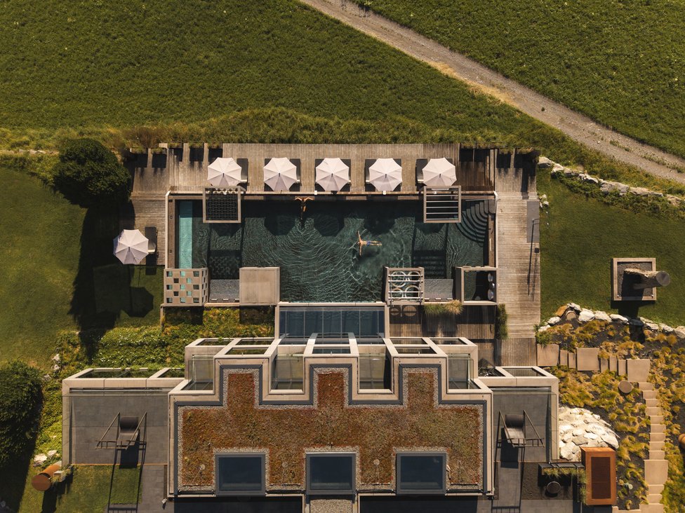Vogelperspektive auf Pool mit Sonnenschirmen und zwei Schwimmern neben modernem Gebäude
