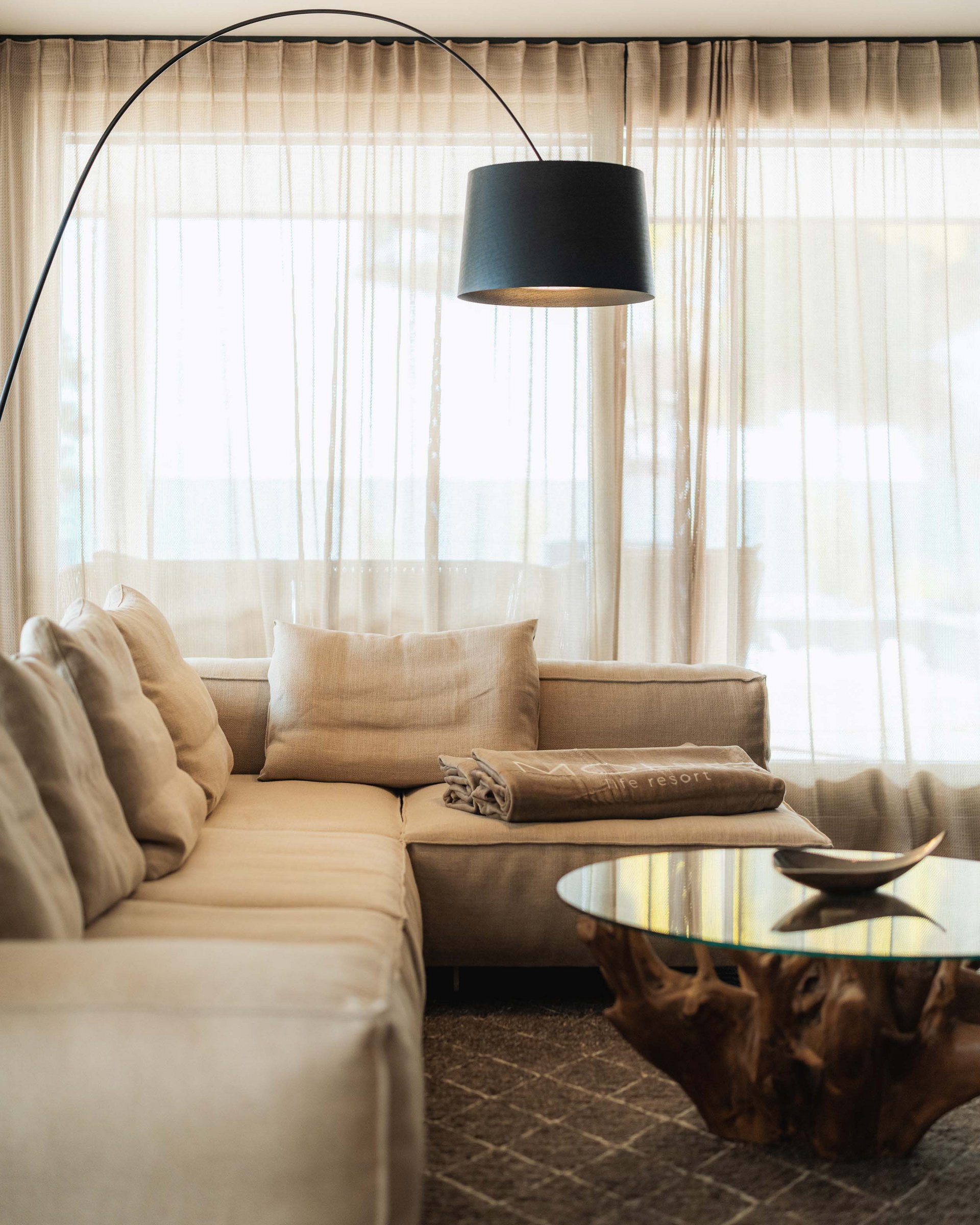Wellness und Luxus: Ihr Hotel in Tirol Beige Wohnzimmersofa mit Kissen und Stehlampe vor Vorhängen