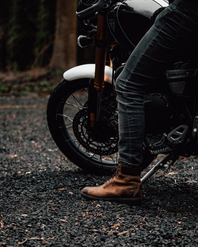 Motorradreifen, Teil des Motorrads und Person mit braunen Stiefeln auf Schotter