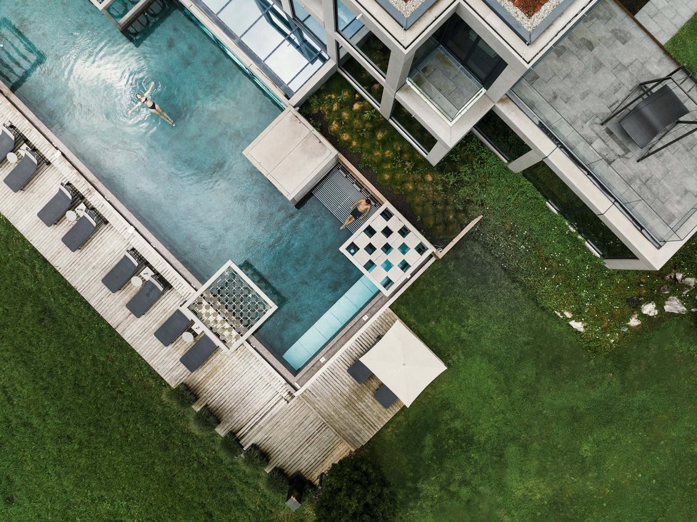 Vogelperspektive auf Pool mit zwei Personen und Liegestühlen an einem modernen Gebäude