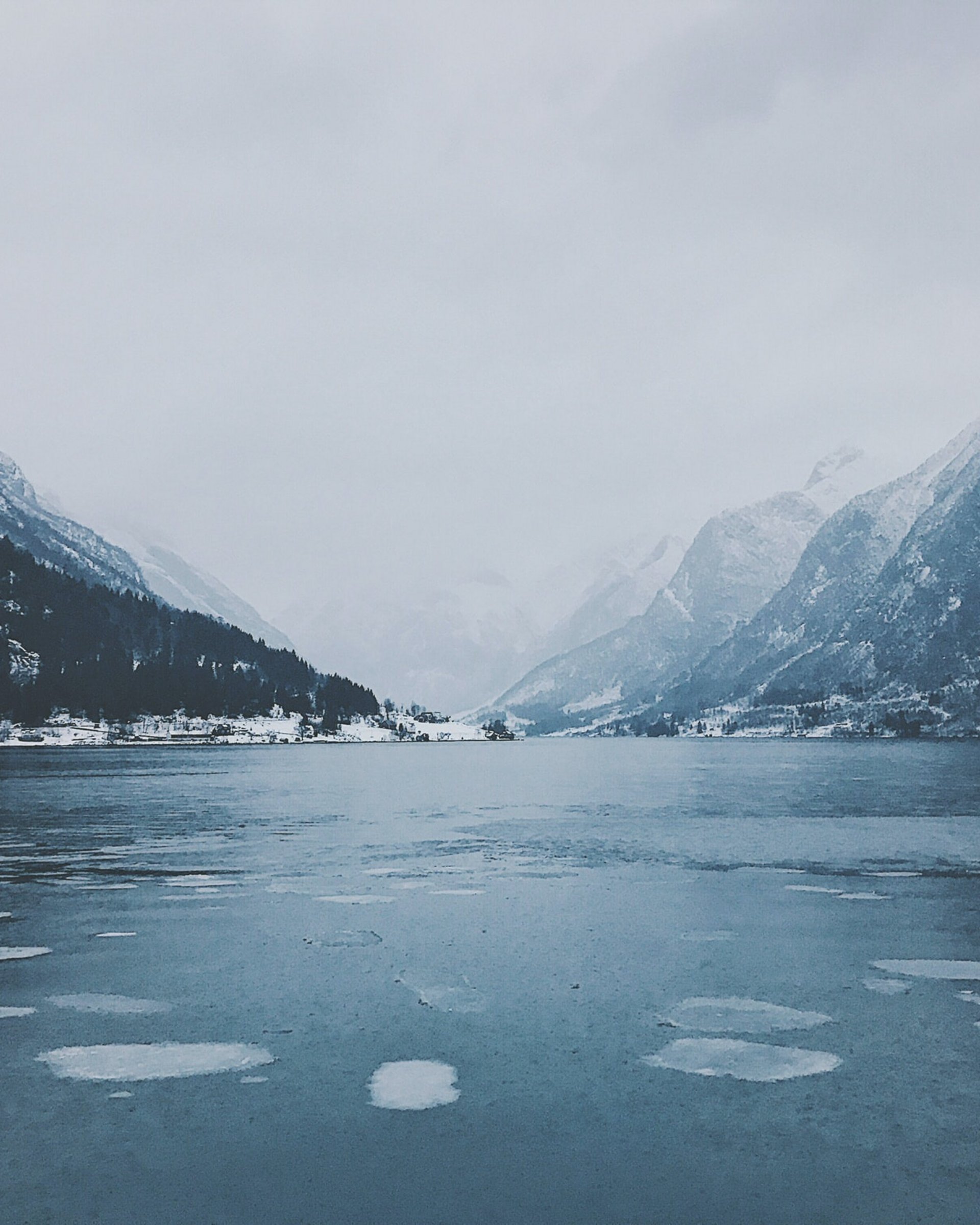 Gefrorener See mit schneebedeckten Bergen und bewölktem Himmel