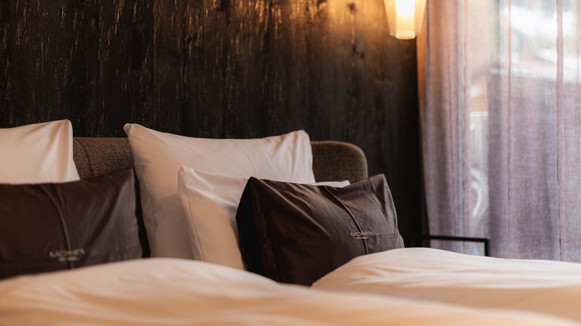 Wellness und Luxus: Ihr Hotel in Tirol Gemütliches Doppelbett mit braunen und weißen Kissen, warme Beleuchtung