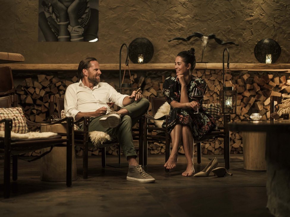 Wellness und Luxus: Ihr Hotel in Tirol Paar sitzt entspannt in gemütlicher Bar mit Holz, trinkt Wein und lacht