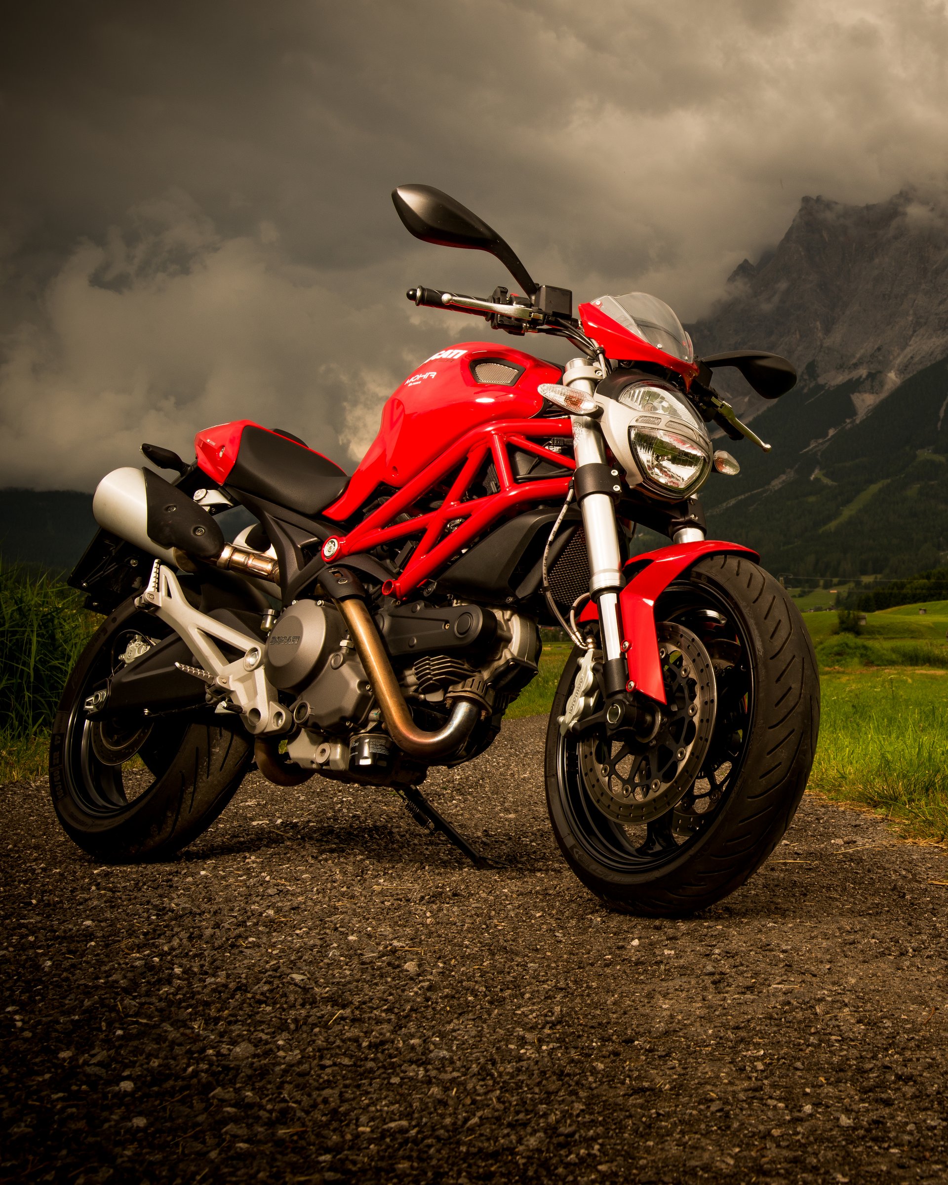 Rotes Motorrad auf Landstraße mit Berg und wolkigem Himmel im Hintergrund