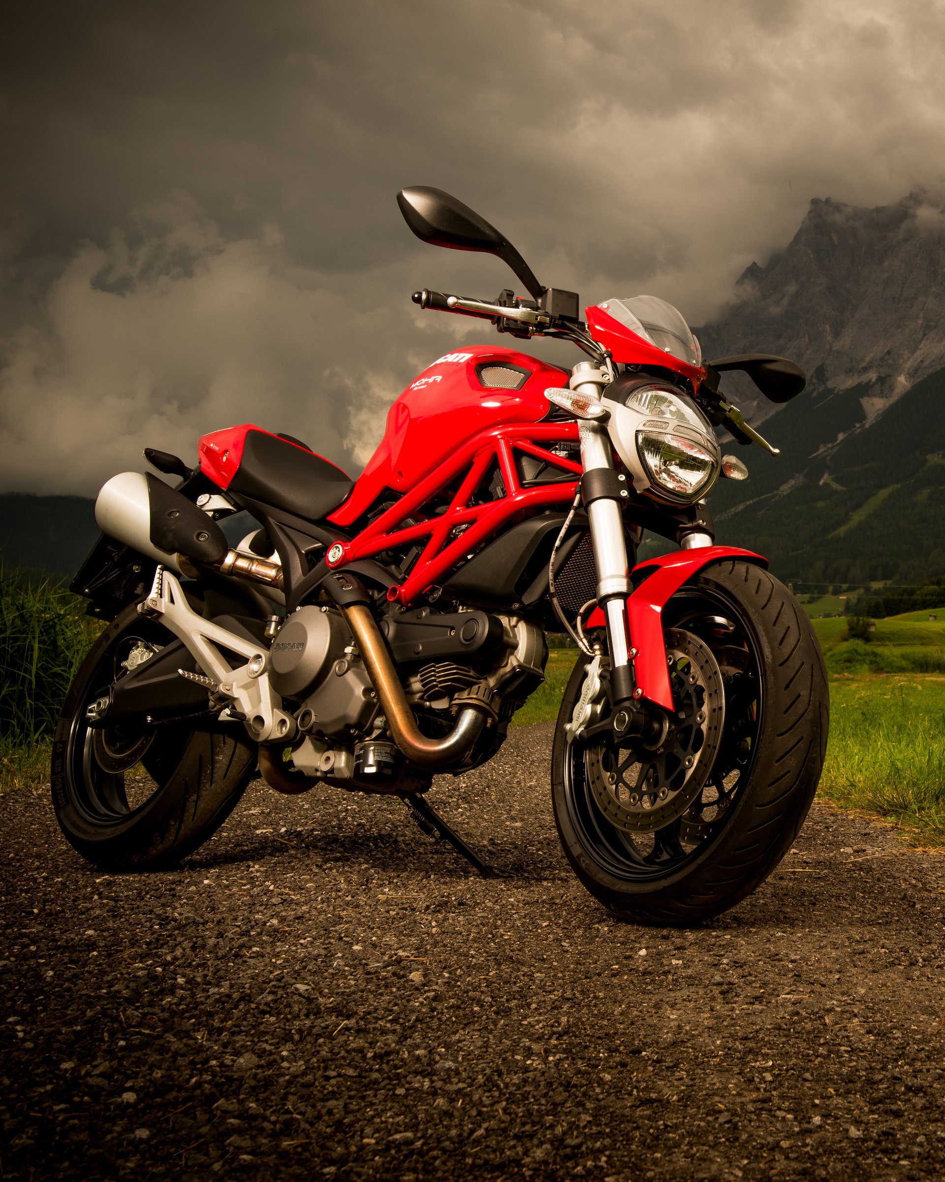 Rotes Motorrad auf Landstraße mit Berg und wolkigem Himmel im Hintergrund