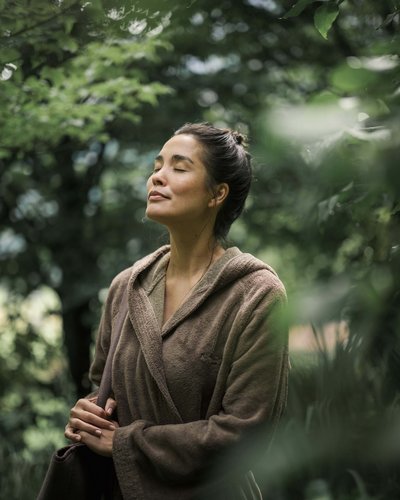 Frau in braunem Bademantel entspannt sich draußen mit geschlossenen Augen