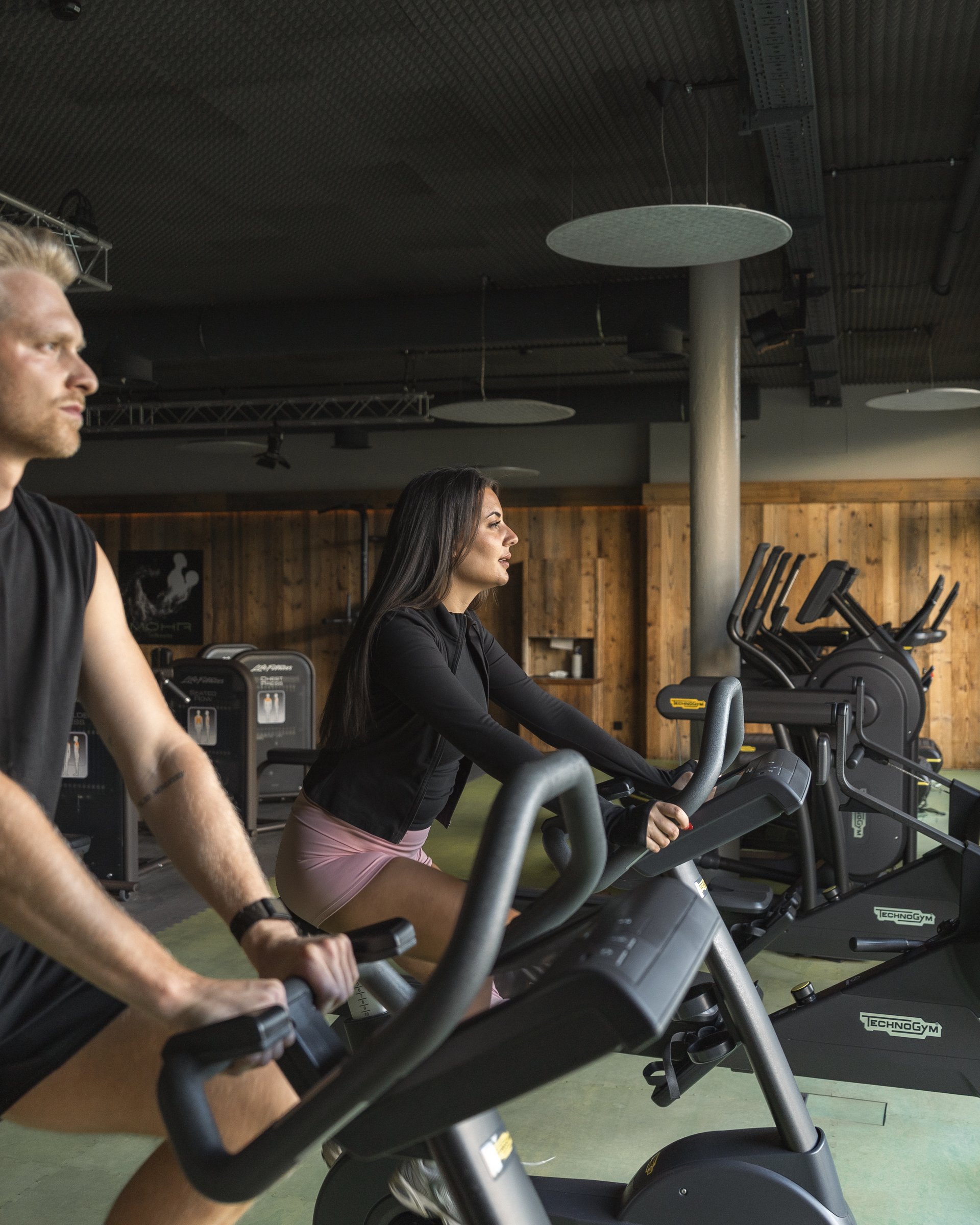Zwei Personen trainieren auf Fahrradergometern in einem Fitnessstudio