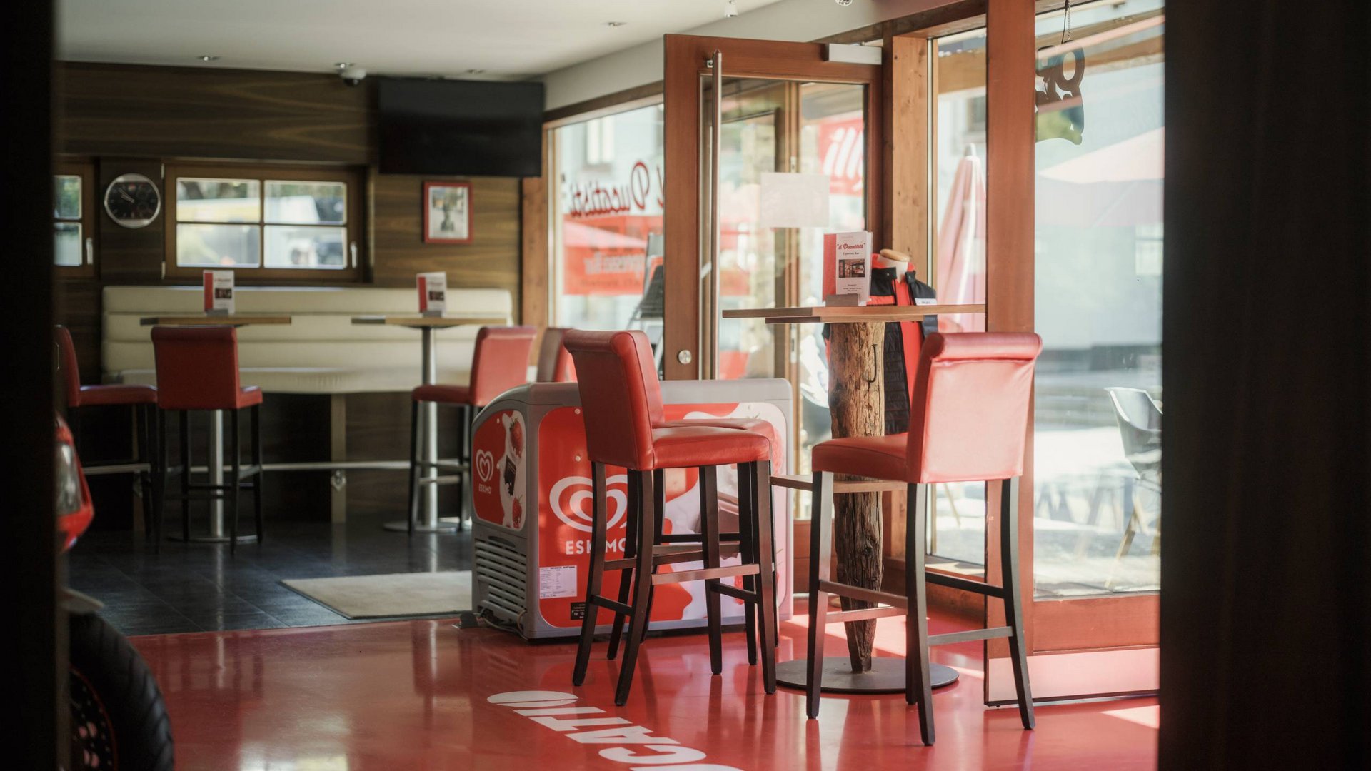 Innenansicht eines Cafés mit roten Barhockern und Tischen bei Tageslicht