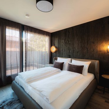 Modernes Schlafzimmer mit Doppelbett, dunkler Akzentwand und Vorhängen am Fenster