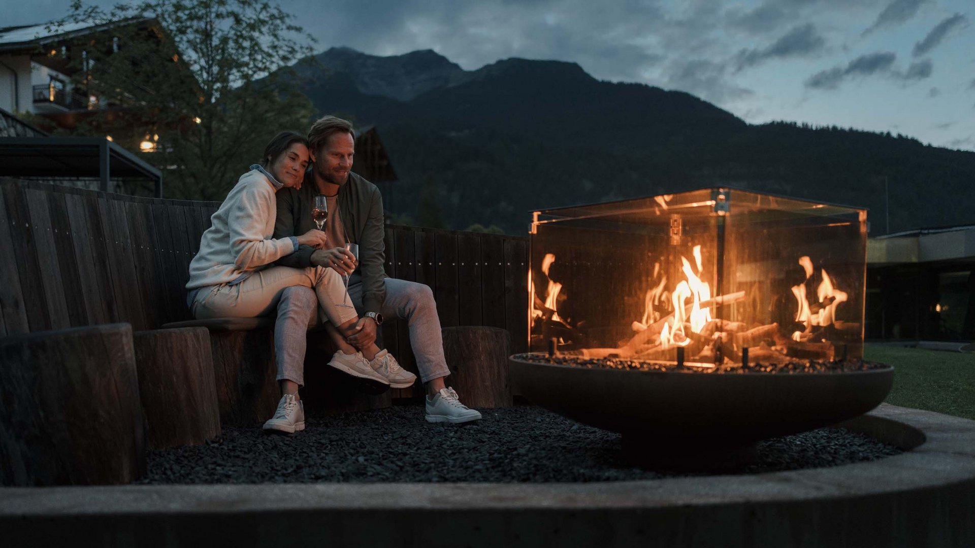 Paar sitzt abends entspannt am Feuer mit Bergblick