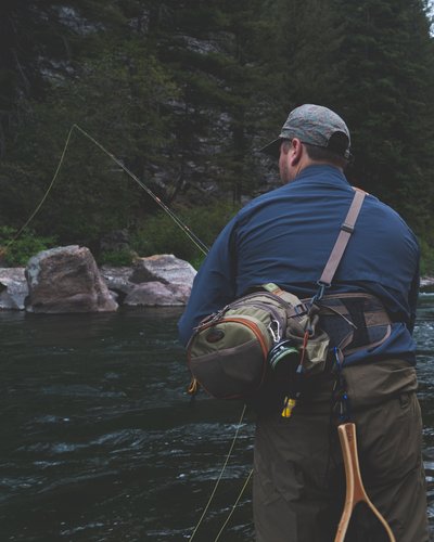 Wellness und Luxus: Ihr Hotel in Tirol Mann beim Fliegenfischen am Bachufer in bewaldeter Berglandschaft